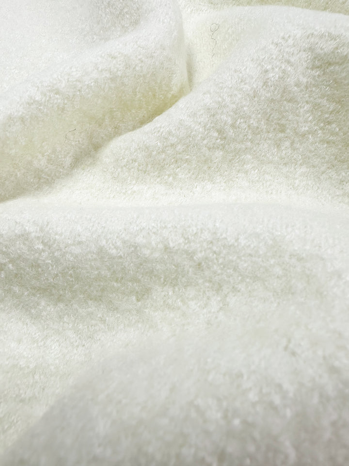 Close-up of Super Cheap Fabrics' Boiled Wool in Ivory. This 150cm blend has a soft, fluffy texture with gentle folds. The light reflects off tiny fibers, showcasing its warm, cozy surface and creating depth and comfort.