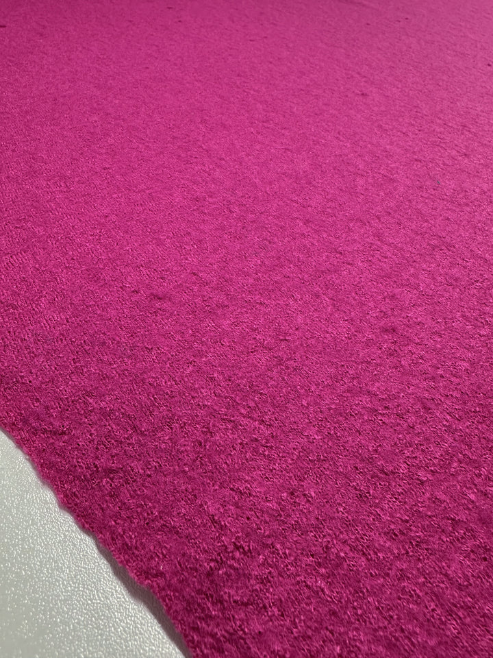 A close-up of the Boiled Wool fabric by Super Cheap Fabrics, in a vibrant Fuchsia Red color, showcases its rough texture. The evenly colored surface stretches smoothly across the frame, maintaining a consistent shade of pink throughout.