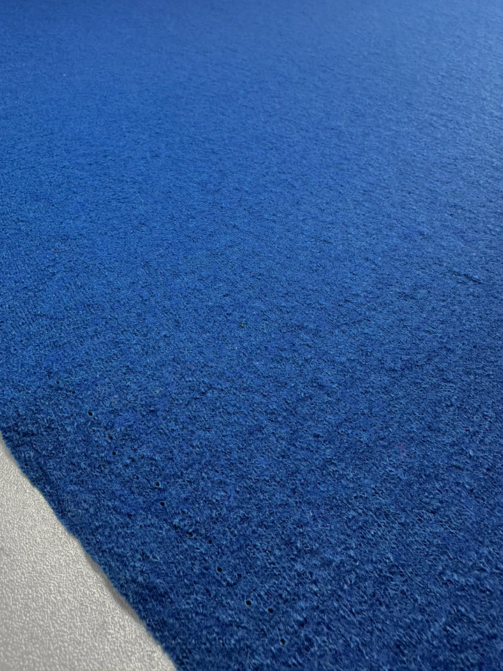 The Boiled Wool - Lapis Blue from Super Cheap Fabrics features a textured surface resembling heavy-weight wool, with a rich blue top half transitioning to a light gray bottom edge, evoking the feel of velvety material and showcasing subtle variations in blue tones. Width: 150cm.