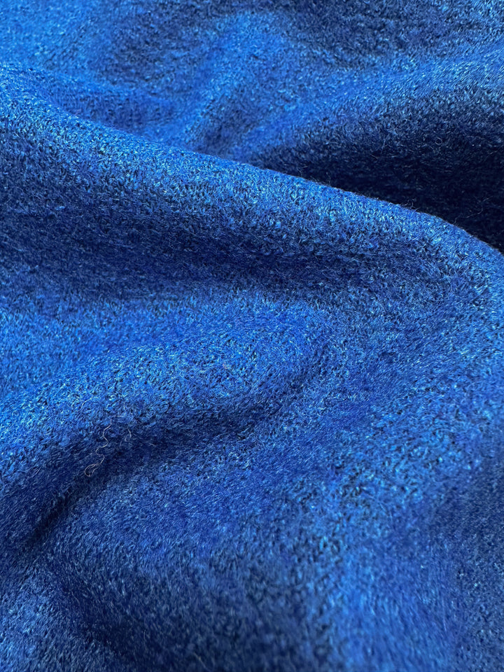 Close-up of a Boiled Wool - Lapis Blue fabric from Super Cheap Fabrics, showcasing a deep blue hue with soft folds and a slightly fuzzy surface. The visible weave highlights rich color variations for a cozy, tactile appeal. Width: 150cm.