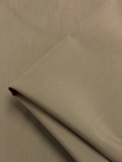 A folded piece of olive green fabric, Poplin - Safari - 148cm by Super Cheap Fabrics, rests on a flat surface. Soft lighting accentuates its smooth texture, highlighting the lightweight polyester-cotton blend’s refined appearance that's perfect for crafting garments.