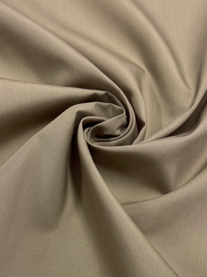 A close-up of the Poplin - Safari - 148cm from Super Cheap Fabrics, featuring its smooth texture and soft drape in a spiral pattern.