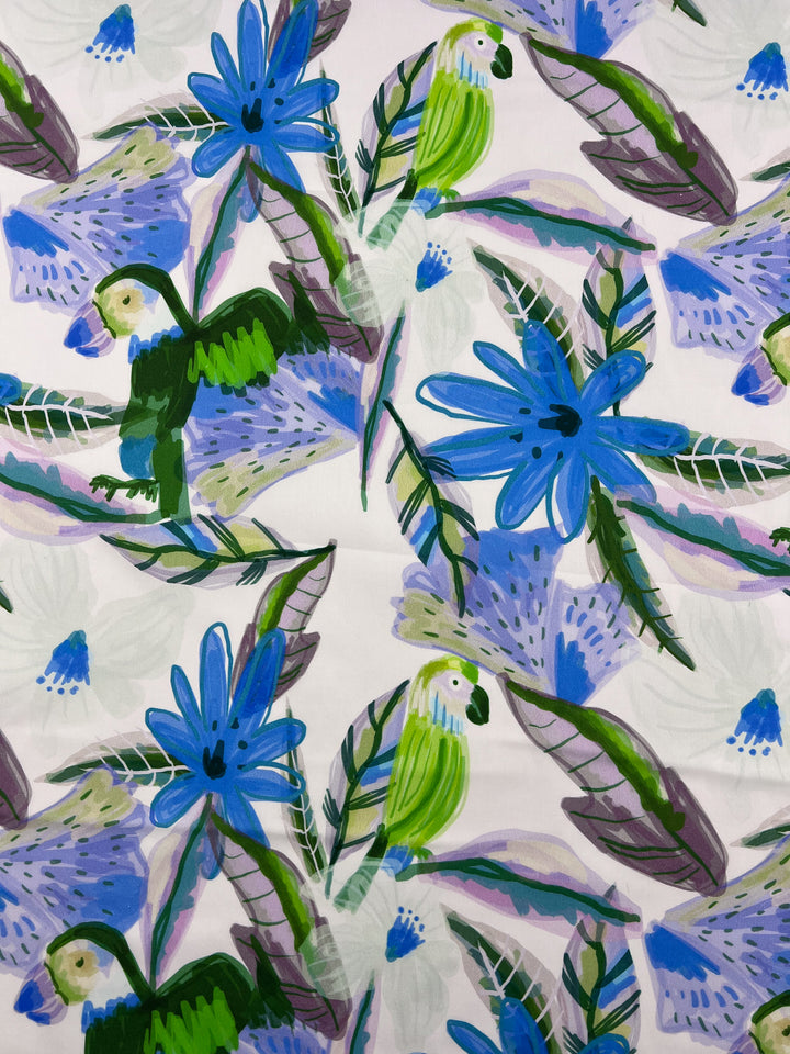 Super Cheap Fabrics' Printed Cotton - Blue Paradise - 150cm has a vibrant pattern with blue flowers, green parrots, and abstract green, purple, and blue leaves on a white background.