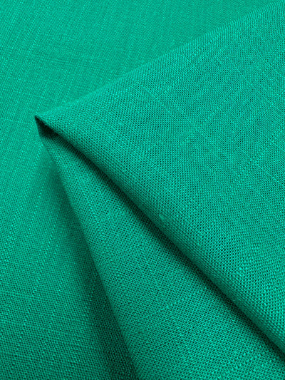 A close-up of folded Super Cheap Fabrics' Linen Blend - Sea Green - 135cm with a slightly textured weave. The fabric's vibrant color and pattern are accentuated by the fold, highlighting its smooth yet slightly coarse surface—perfect for table linens.