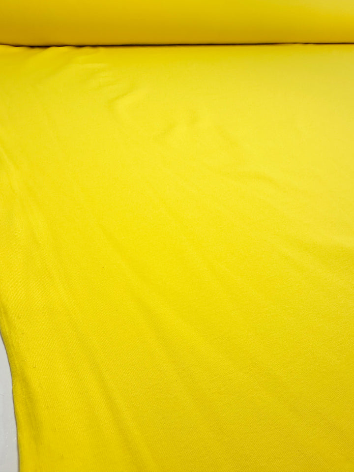 A close-up view of Super Cheap Fabrics' Cotton Lycra in vibrant yellow, spread out smoothly and measuring 170cm.