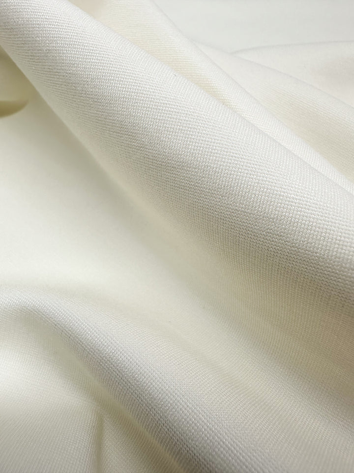 Close-up of Super Cheap Fabrics' Ponte De Roma in Vanilla (155cm) reveals its soft, cream-colored fabric and subtle woven texture. The medium-to-heavy weight material exhibits gentle folds, creating shadows and highlights that enhance its smooth, slightly textured look.