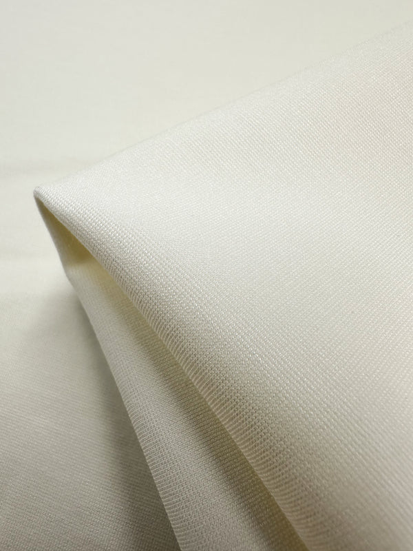 Close-up of folded Ponte De Roma fabric in Vanilla from Super Cheap Fabrics. This 155cm cream-colored material features a smooth, textured surface with a slightly reflective quality and 4-way stretch for versatility.