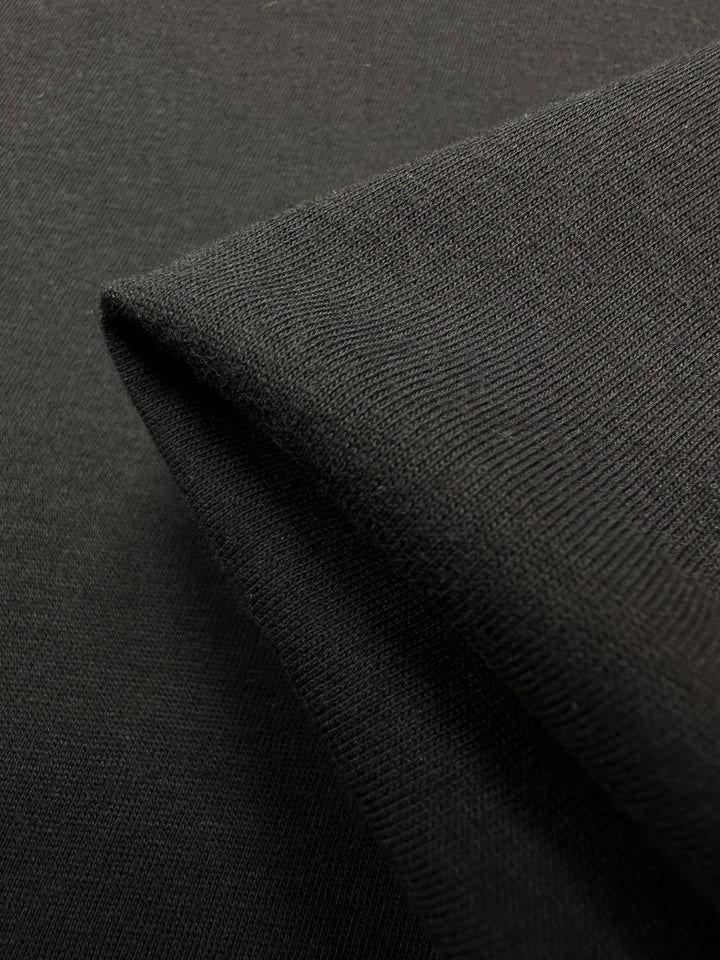 Close-up of a folded piece of black cotton jersey fabric from Super Cheap Fabrics, highlighting its texture and weave.