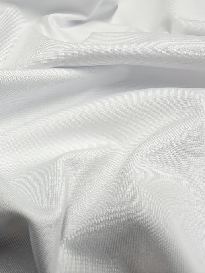 Close-up of Super Cheap Fabrics' Plain Lycra in Snow White, showcasing soft folds and a gentle texture. The light, slightly shiny material creates depth and subtle shadowing across its 160cm-wide surface, similar to high-quality activewear.