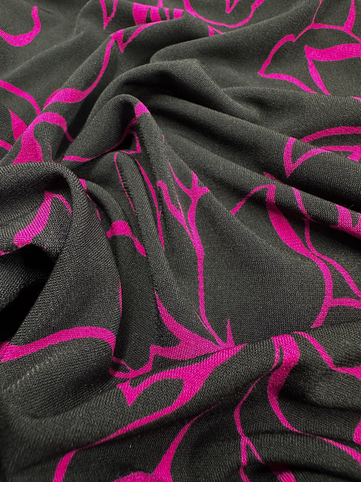 A close-up of Super Cheap Fabrics’ Printed Lycra - Devour reveals its intricate pink abstract floral patterns on black. The slightly wrinkled texture highlights the flexibility of the 145cm wide, two-way stretch Polyester/Spandex blend.