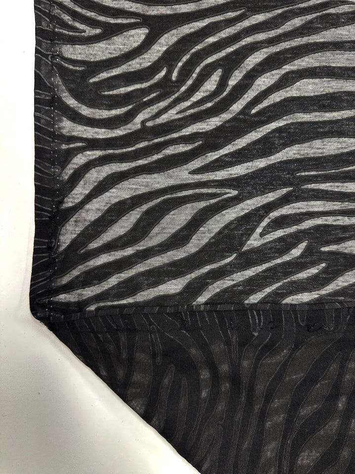 Close-up of Super Cheap Fabrics' Burnout Jersey - Zebra (160cm) with a black and gray zebra stripe. The textile layers reveal sheer and opaque sections, with a folded lower left corner showcasing texture and design contrast.