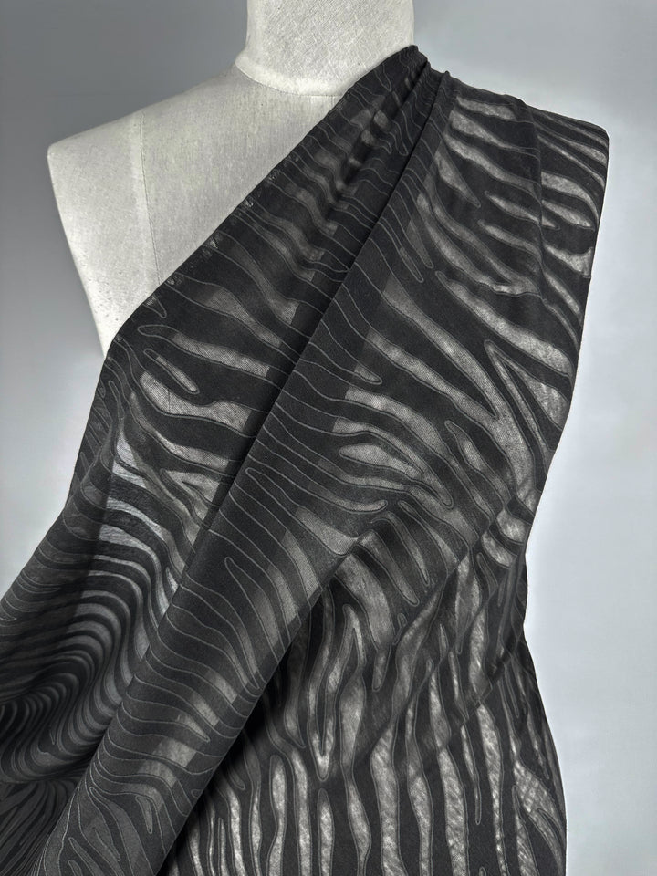 The black and gray Burnout Jersey - Zebra from Super Cheap Fabrics features a smooth, flowing design with a wavy zebra-like pattern on a neutral 160cm backdrop, creating an elegant sense of movement.