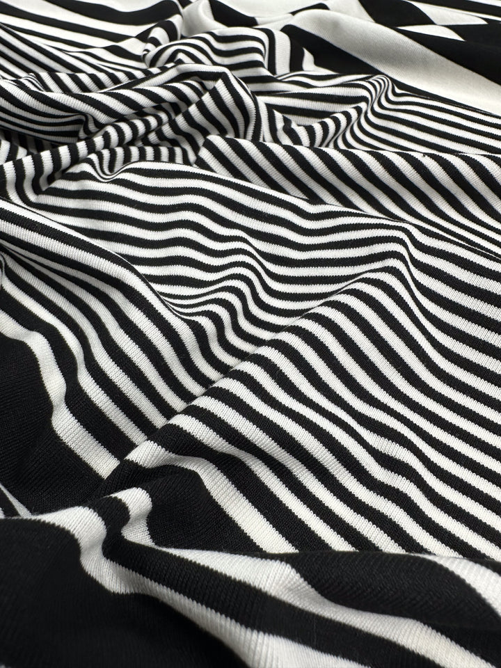 Close-up of Super Cheap Fabrics’ Viscose Jersey - Paralello - 160cm, showcasing black and white stripes that ripple and fold, creating an optical illusion. The lightweight, stretchy material enhances texture and fluidity, adding depth to the visual effect.