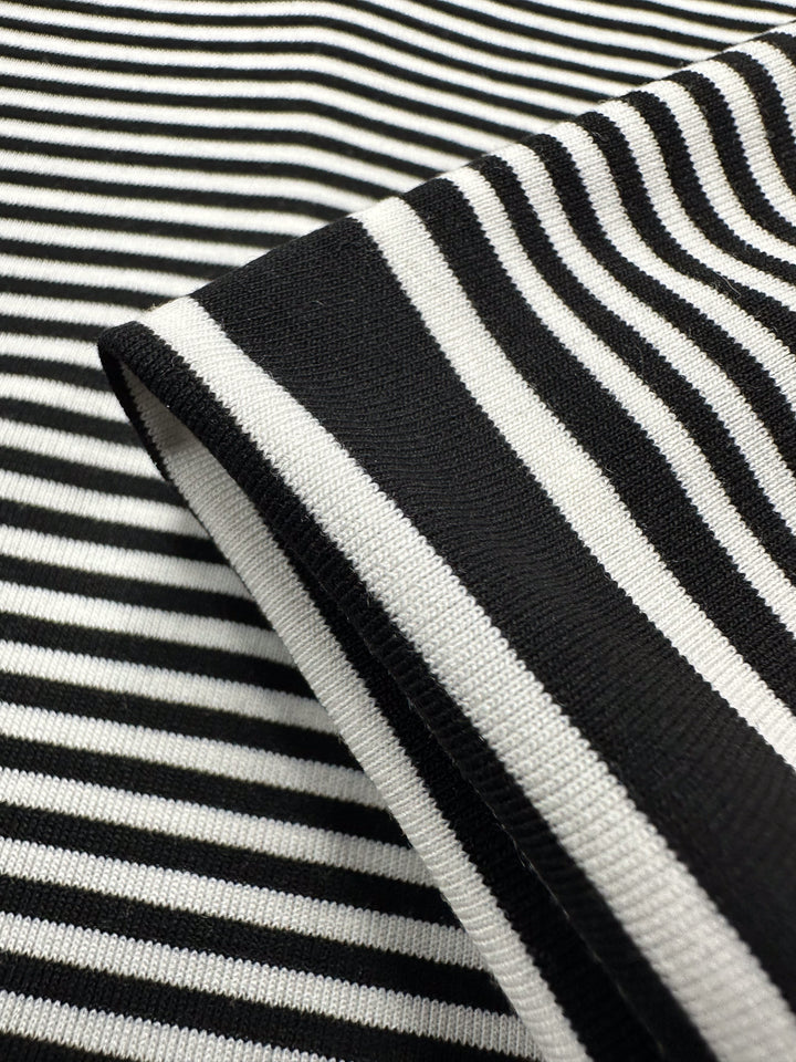 Close-up of the black and white Viscose Jersey - Paralello fabric from Super Cheap Fabrics, featuring contrasting horizontal and vertical stripes. The lightweight 160cm viscose blend is folded to highlight its soft, stretchy texture and varied stripe directions.