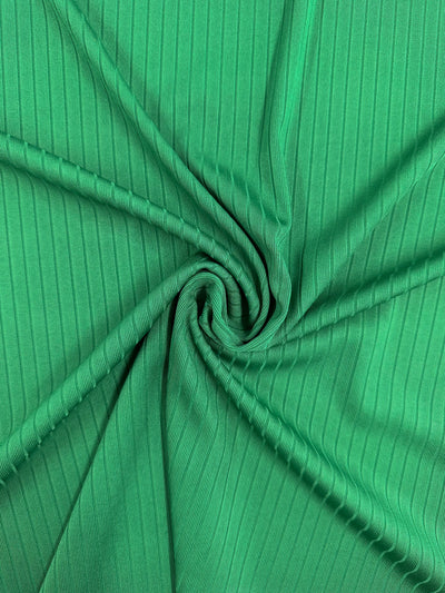 Close-up of Super Cheap Fabrics' Rib Knit - Abundant Green - 177cm, swirled in the center for a spiral effect. The texture highlights visible vertical ribbing and generous stretch.