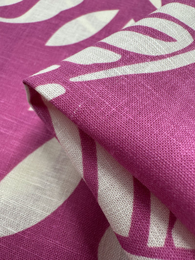 Close-up of Super Cheap Fabrics' Linen Blend in Rose Violet (138cm), featuring a folded lightweight fabric with woven details and white abstract shapes against a pink background, showcasing its breathable texture.