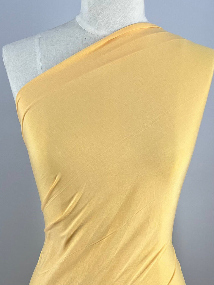 A mannequin dressed in asymmetrically styled Summer Cotton Knit - Sunset Gold fabric from Super Cheap Fabrics, posed against a plain gray background.