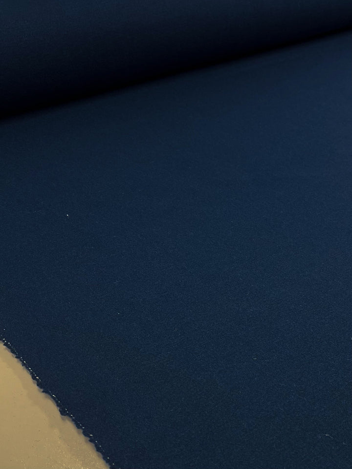 A close-up of a Wool Cashmere - Navy Peony - 150cm fabric roll by Super Cheap Fabrics. This extra heavy weight wool fabric, unrolled across a flat surface with the roll visible at the top, showcases its smooth and evenly colored texture—ideal for outer coats. Dry clean only.