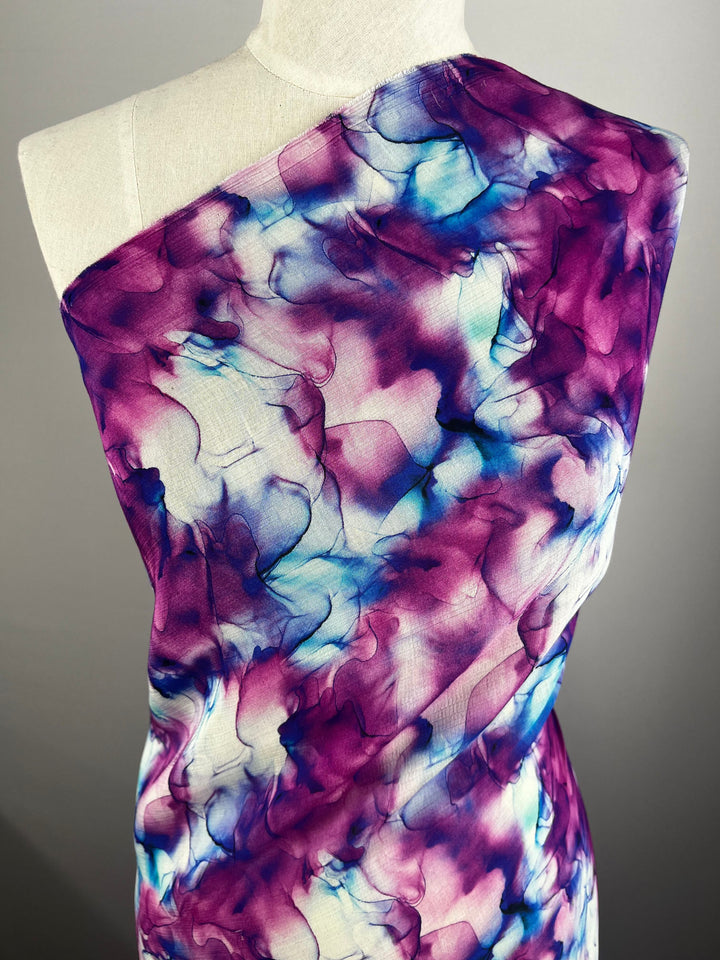 A mannequin showcasing the Designer Cotton - Celeste - 150cm by Super Cheap Fabrics, adorned with a vibrant and abstract pattern in shades of purple, blue, and white. This breathable fabric has a watercolor-like appearance with smooth, flowing transitions between colors—perfect for luxury sewing projects.