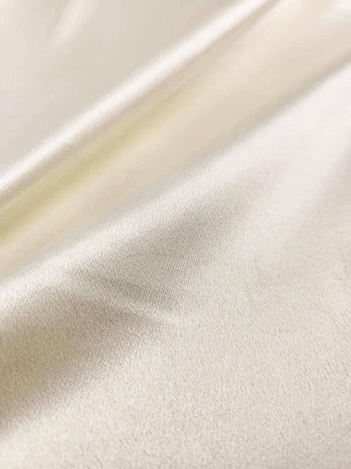 Close-up of Super Cheap Fabrics' Satin Back Crepe in cream, showing its smooth texture and glossy finish with subtle folds—perfect for elegant tops or eveningwear, width 150cm.