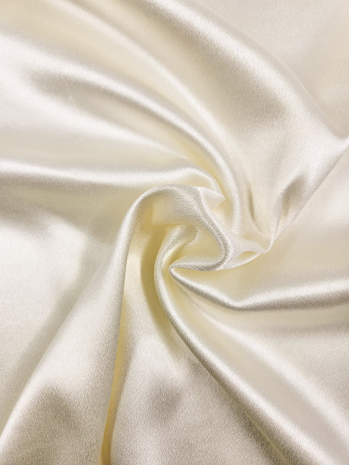 A close-up of the Super Cheap Fabrics' Satin Back Crepe - Cream 150cm fabric, displaying its smooth, shiny surface in gentle folds. The light enhances its glossy texture and softness, ideal for crafting elegant tops and eveningwear.