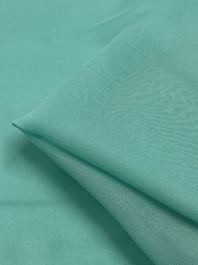 Close-up of a folded piece of Silk Georgette - Lagoon from Super Cheap Fabrics, ideal for spring and summer outfits. The lightweight material appears soft and smooth, with a gentle drape. The image focuses on the fabric's texture and color, showcasing its subtle sheen and even weave.