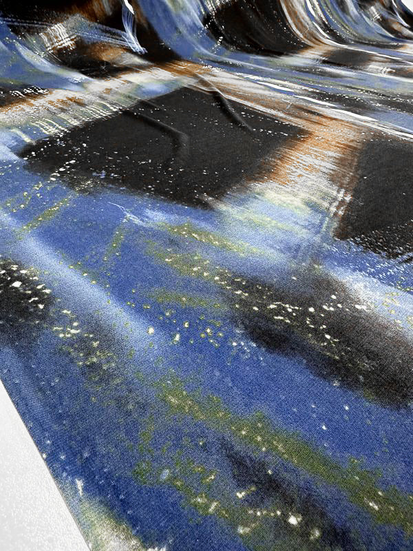 A close-up image of the "Printed Lycra - Astro - 150cm" by Super Cheap Fabrics showcases a dynamic abstract design with streaks and splashes in shades of blue, black, white, and hints of green and brown. The medium-weight fabric appears slightly wrinkled and draped, adding depth and texture to the visual.