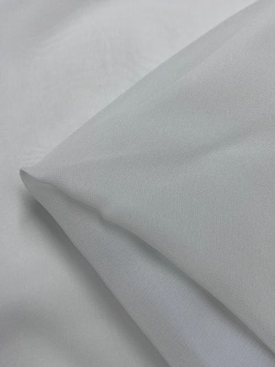 The Pure Silk Georgette in Silver Blue from Super Cheap Fabrics showcases a delicate texture and fine weave, ideal for spring and summer outfits. Its lightweight nature is evident with a slight fold at one corner. Width: 135cm.