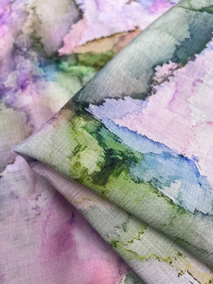 Close-up of Super Cheap Fabrics' Designer Cotton - Pastel - 150cm, featuring a luxury watercolor pattern in pastel shades of pink, purple, green, and blue. The abstract design suits sewing projects, with the layered fabric showcasing a soft, flowing texture.