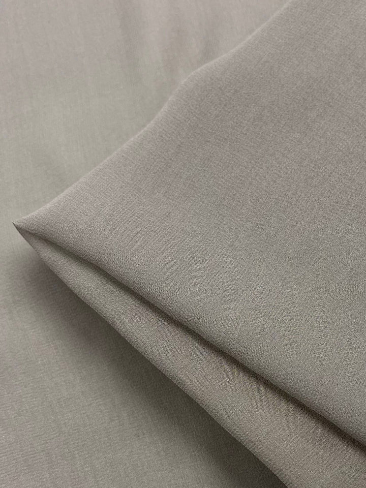 A close-up view of the Earth Silk Georgette fabric by Super Cheap Fabrics, folded at the corner, highlighting its smooth texture and subtle weave—perfect for spring and summer outfits. The light gray tone adds an elegant touch to any ensemble.