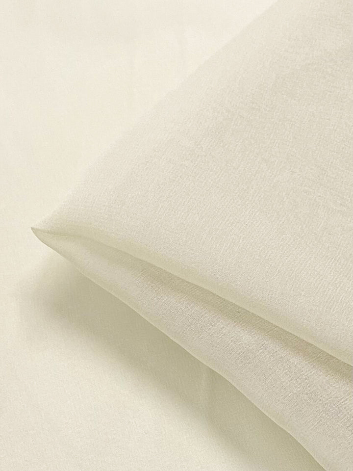 A close-up image of a folded piece of smooth, white Silk Georgette - Champagne - 135cm fabric by Super Cheap Fabrics. The material appears soft and lightweight with a subtle sheen and slightly translucent texture, ideal for creating summer outfits. The fold creates gentle shadows, emphasizing the fabric's delicate quality.