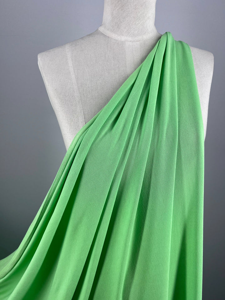 A mannequin is draped with the Paradise Green fabric, "Summer Cotton Knit - Paradise Green - 170cm" by Super Cheap Fabrics. It elegantly wraps the torso on a plain gray backdrop, showcasing its smoothness and vibrant hue with excellent stretch recovery.