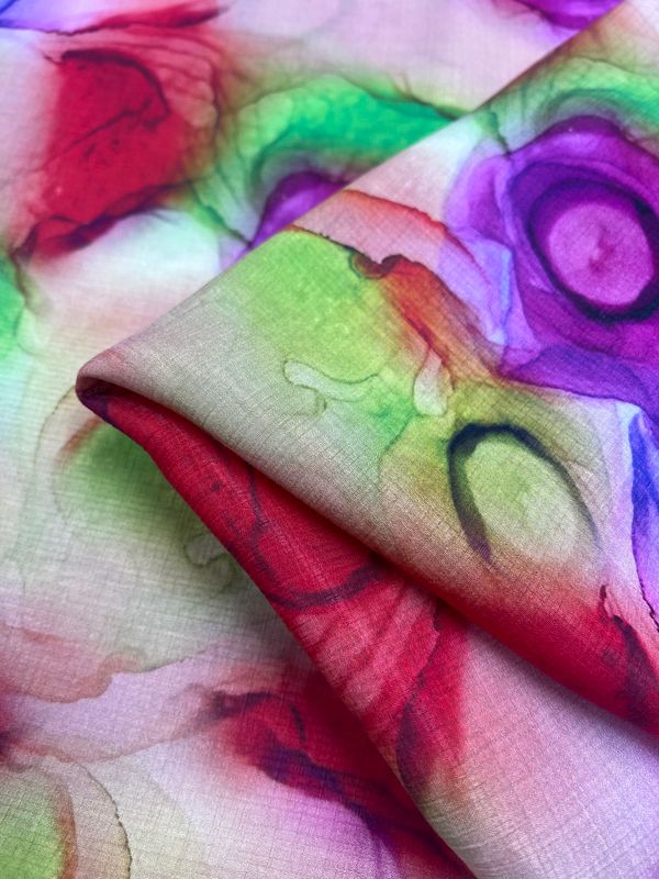 A close-up of Super Cheap Fabrics' "Designer Cotton - Springs - 150cm" showcases vibrant watercolor swirls in red, purple, green, and blue. Ideal for luxury sewing projects, the fabric is slightly folded along one edge to highlight its colorful abstract pattern.