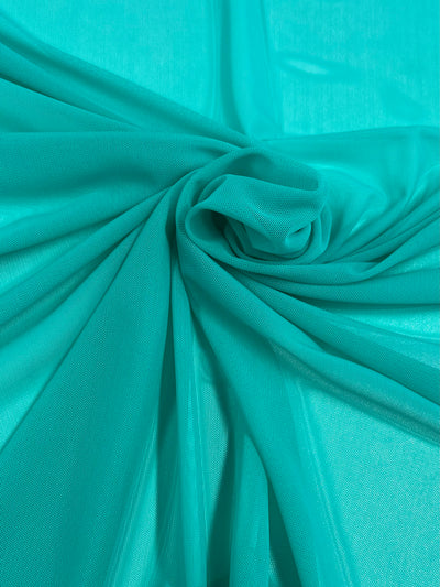 The Pool Green Plain Mesh from Super Cheap Fabrics features a lightweight material elegantly arranged with folds gathered in a central knot, adding movement and texture to the smooth 155cm polyester surface.