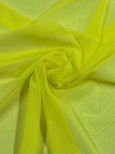 A close-up of the Super Cheap Fabrics' "Plain Mesh - Yellow Plum - 155cm" reveals bright yellow polyester with a soft, semi-sheer texture, gathered in the center to form gentle folds and a swirling pattern, indicating its potential for creative or fashion projects.