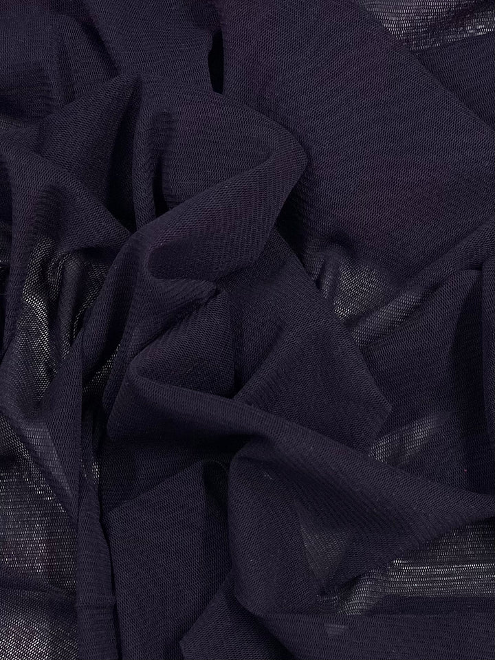 A close-up of Super Cheap Fabrics' Plain Mesh in Vintage Violet reveals its crumpled dark purple mesh with a glossy look. The lightweight polyester's intricate folds and translucent quality create dynamic textures, showcasing subtle light and shadow variations. Width: 155cm.