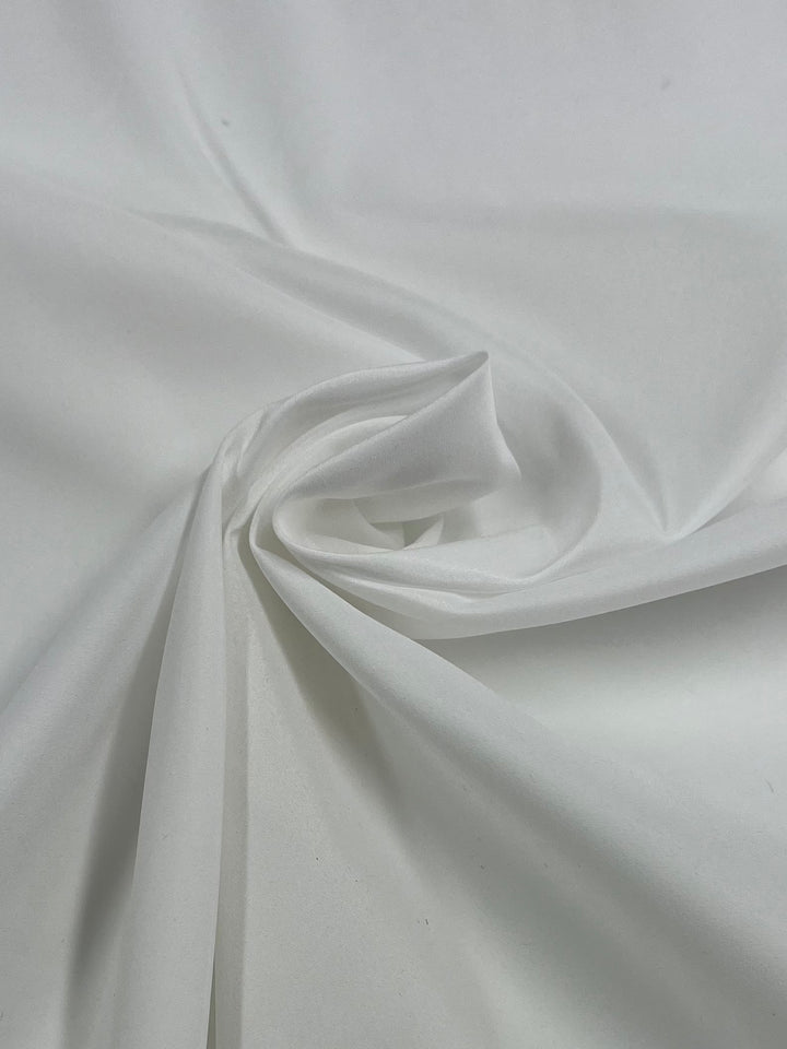 A close-up image of a white fabric with a smooth texture, twisted gently at the center to form soft folds and a subtle spiral design. The lightweight Lining - White - 150cm from Super Cheap Fabrics creates an elegant, minimalistic aesthetic perfect for refined tailoring.