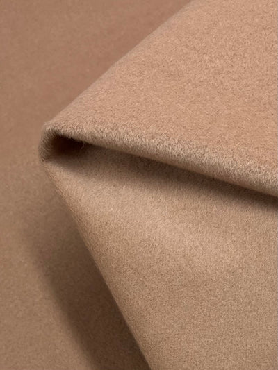 Close-up of a folded piece of soft beige fabric, showcasing its smooth and plush texture. The heavyweight fabric appears to be thick and of high quality, with a slight sheen that highlights its softness. This luxurious material is Super Cheap Fabrics' Wool Cashmere - Maple Sugar - 150cm in a charming maple sugar hue.