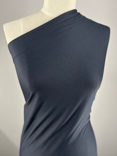 A mannequin is draped in a single-shoulder, dark navy fabric that wraps snugly around the torso. The background is plain and neutral, highlighting the texture and drape of Super Cheap Fabrics' Interlock - Dark Navy - 150cm.