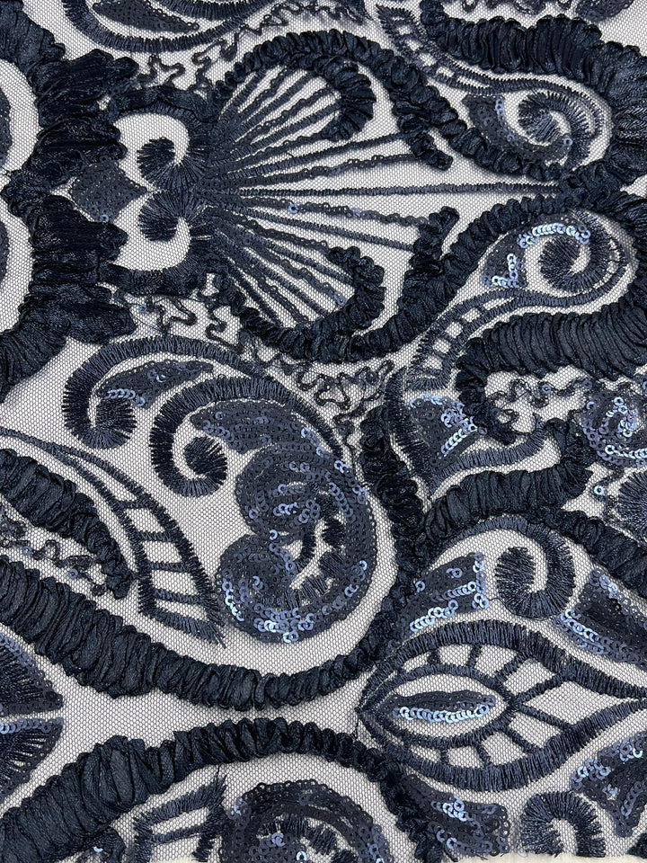 Close-up view of an intricate black lace fabric with an ornate pattern. The medium weight fabric features a combination of floral and swirling designs adorned with shimmering sequins, giving it a textured and elegant appearance. The sheer base, made from 100% polyester, enhances the detailed design. This is the "Evening Lace - Night Shade - 150cm" by Super Cheap Fabrics.