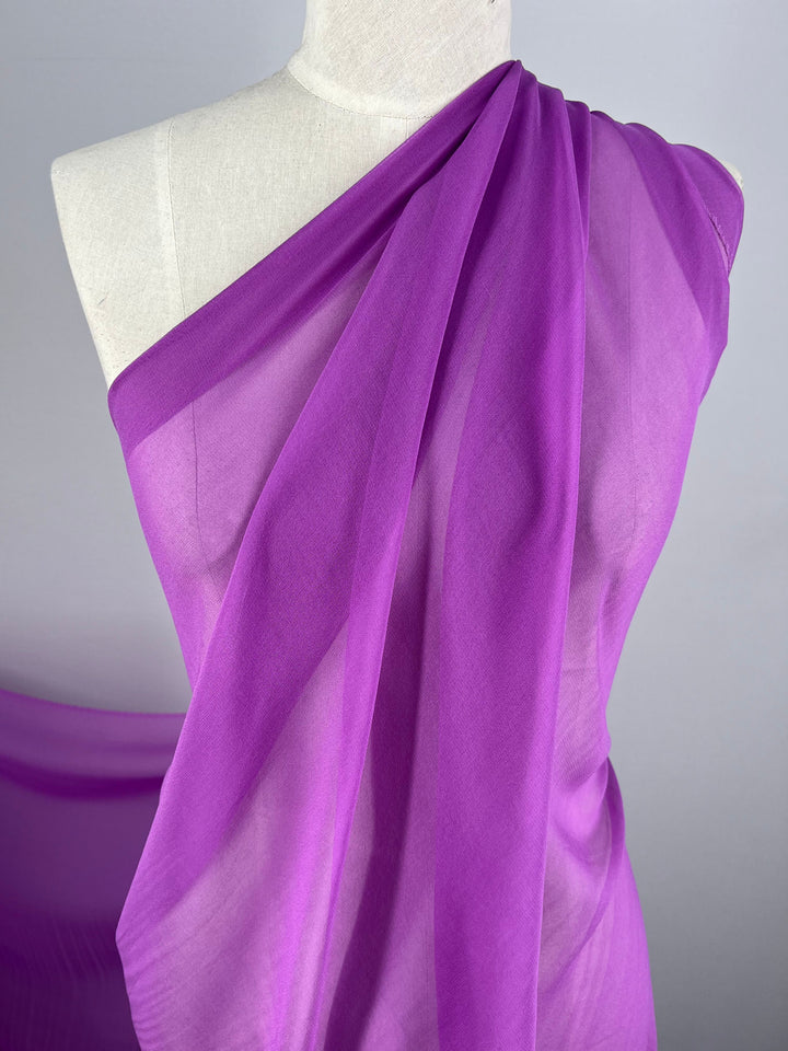 A mannequin draped in the Iris-colored Silk Georgette from Super Cheap Fabrics, beautifully covering one shoulder and crossing diagonally over the torso. The lightweight fabric, measuring 135cm, is perfect for spring and summer outfits. The backdrop is a plain light grey color, highlighting the vibrant, semi-transparent material.