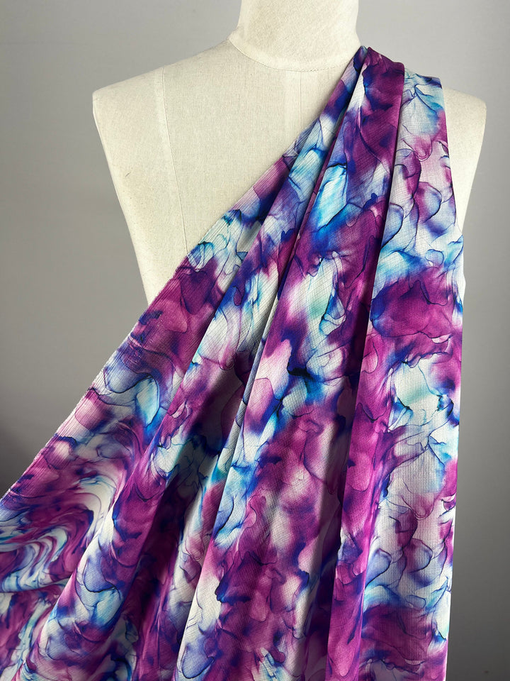 A white mannequin adorned with the Designer Cotton - Celeste fabric from Super Cheap Fabrics, featuring a breathable material with a vibrant abstract pattern of swirling purples, blues, and pinks on a white background. This exquisite fabric is perfect for luxury sewing projects, highlighting designer cotton at its finest.