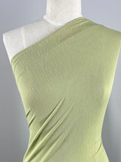 Close-up of a mannequin wearing the Summer Cotton Knit top in Beechnut by Super Cheap Fabrics. The light green, single-shoulder design is crafted from a lightweight knit fabric, draping smoothly across the torso against a neutral grey background.