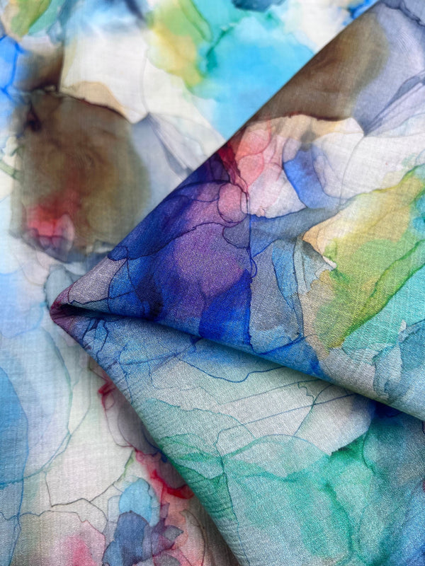 A close-up of the Designer Cotton - Bluness from Super Cheap Fabrics, showcasing watercolor-style patterns in vibrant blues, greens, purples, and pinks. Layered to highlight its delicate texture and intricate design, this luxury fabric beautifully complements high-end sewing projects.