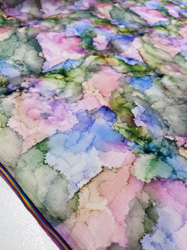 A close-up of Super Cheap Fabrics' Designer Cotton - Pastel - 150cm reveals a colorful tie-dye effect. It showcases soft blends of pink, blue, green, and purple on designer cotton for an organic look. Ideal for luxury sewing projects, it has a slightly glossy texture with thin rainbow edge stripes.