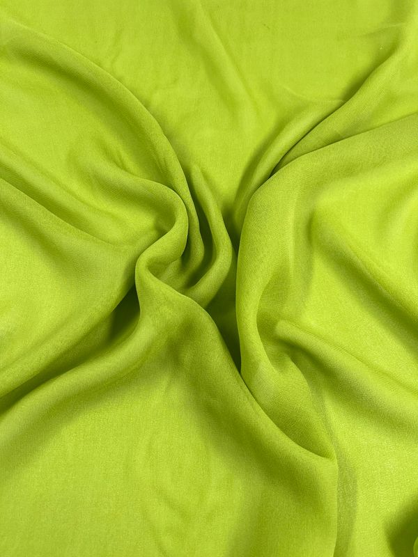 A close-up of Super Cheap Fabrics' Silk Georgette - Evergreen fabric showcases its vibrant green color and soft texture. Loosely gathered in the center, it creates gentle folds and curves that give it a flowing, dynamic appearance. The bright, uniform color emphasizes the smoothness of this lightweight spring-summer fabric measuring 135cm in width.