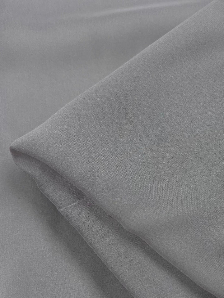 A close-up view of a folded piece of smooth, light gray Pure Silk Georgette - New Marble by Super Cheap Fabrics, 135cm wide.