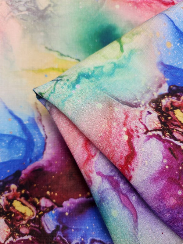 A detailed view of the Designer Cotton - Saphira - 150cm from Super Cheap Fabrics reveals a dynamic mix of colors such as blue, pink, green, and purple in an abstract watercolor design. Perfect for luxury sewing projects, this high-quality fabric is elegantly folded to highlight its smooth texture and intricate color patterns.