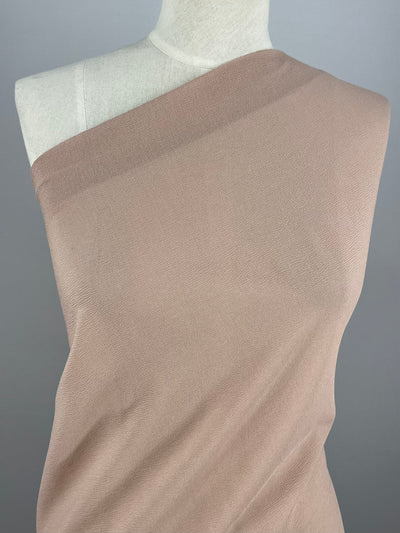 A mannequin displays a medium-weight fabric from Super Cheap Fabrics draped around it. The Misty Rose-colored Polyester Broad Cloth, measuring 140cm in width, is wrapped asymmetrically, exposing one shoulder of the mannequin. The plain gray background highlights the fabric's texture and color.