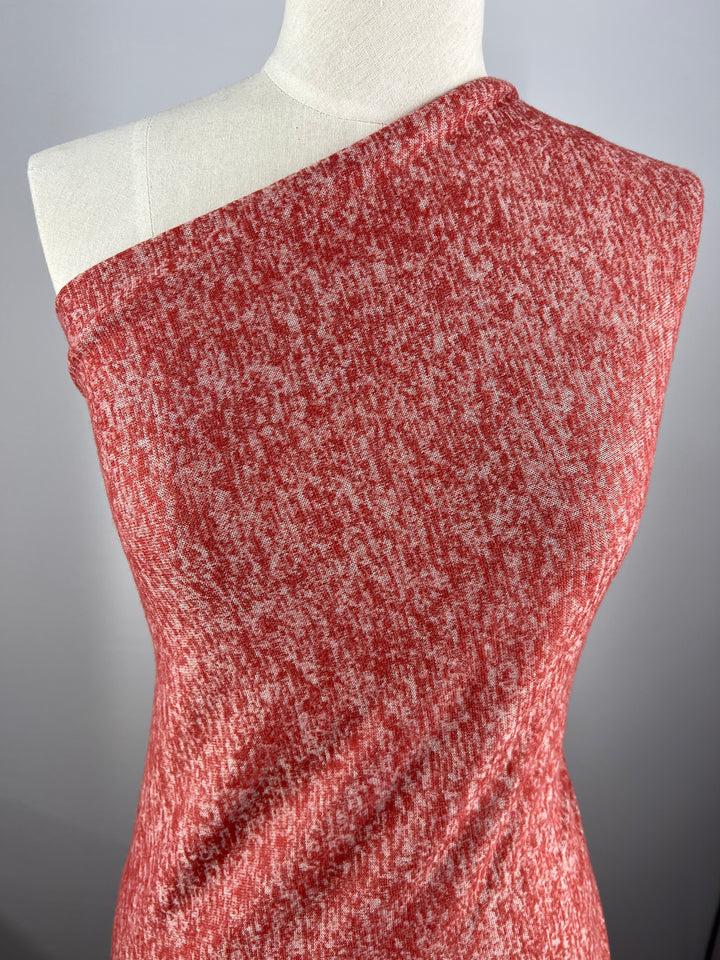 A close-up of a red and white textured dress on a dress form. The dress has a one-shoulder design, revealing the left shoulder and covering the right. Crafted from Marle Textured Knit - Burnt Ochre - 160cm from Super Cheap Fabrics, the heathered medium weight fabric offers both a casual yet chic appearance with generous stretch for comfort.